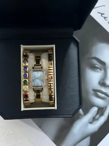 Nahaufnahme einer eckigen Goldene Uhr mit Strasslünette und bunten Armbändern in Box