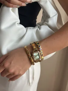 Detailansicht einer goldenen quadratischen Uhr mit bunten Edelstein-Armbändern.