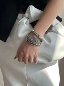 Close-up of silver steel evil eye watch stacked with charm bracelets on wrist.