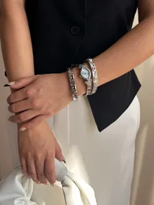 Close-up of stylish silver-tone oval watch and evil eye elastic link bracelets on wrist