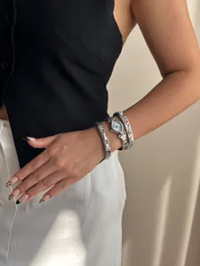 Detailed view of a silver evil eye watch stacked with elastic charm bracelets on arm