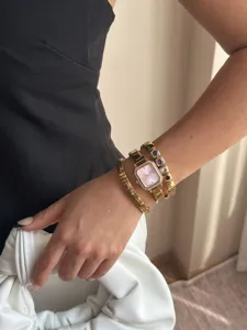 Nahaufnahme der eleganten goldene quadratische Uhr und der bunten Edelsteinarmbänder im Set