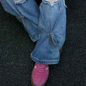 Dettaglio di jeans strappati blu chiaro con spilla a catena con nappine a croce