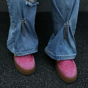 Dettaglio spilla da balia a croce con catena a nappa su jeans in denim blu scuro