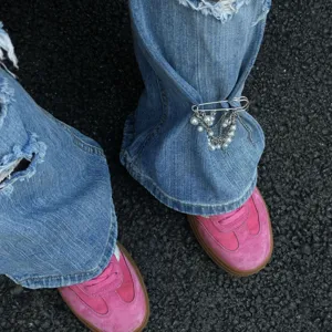 Dettaglio di una spilla da balia argentata con nappe di perle su jeans blu denim