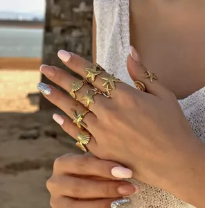 Detaillierte Nahaufnahme vergoldeter Seestern- und Muschelringe an einer Hand am Strand
