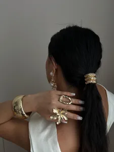 Model draagt een gehamerde gouden armband met dikke ringen en stijlvol haaraccessoire