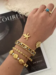 Nahaufnahme von goldenen Edelstahl-Armbändern mit Seestern- und Muscheldesign