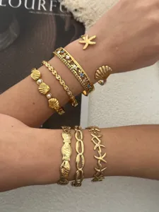 Nahaufnahme von goldenen Meeresarmbändern aus Edelstahl mit Seestern- und Muscheldetails.