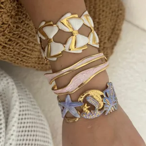 Nahaufnahme von Emaille-Armbändern mit Seestern- und Schleifenmotiven am Handgelenk