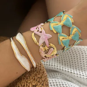 Nahaufnahme von bunten Emaille-Armbändern mit Seestern- und Schleifendesigns am Arm