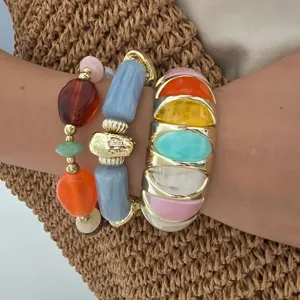 Detail van gestapelde kleurrijke macaron stenen armbanden met gouden accenten