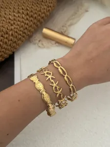 Detailansicht von goldenen Edelstahlarmbändern mit Seestern- und Fischmotiven im Meer-Stil.