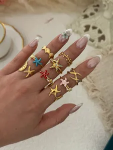 Eine Kollektion goldener Ringe mit Seestern- und Muschelmuster an einer Hand getragen.