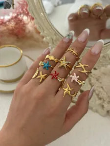 Detailansicht von goldenen Seestern- und Muschelringen im Meeresdesign an der Hand