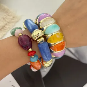 Detailopname van kleurrijke macaron-stenen armbanden en een gouden brede armband