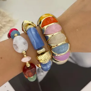Close-up van gestapelde macaron gekleurde stenen armbanden en gouden brede manchet