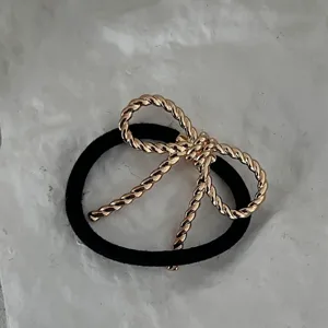 Nahaufnahme einer minimalistischen, goldfarbenen Haarschleife am schwarzen Gummiband.