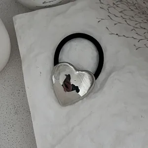 Nahaufnahme eines minimalistischen polierten silbernen Herz-Haargummis auf Stein.