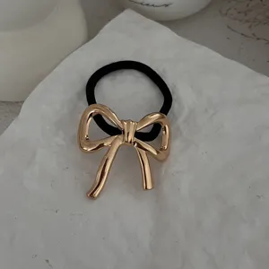Detailansicht eines goldenen Haargummis mit Metallschleife auf weißem Strukturblock.