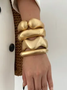 Detailed close-up of a set of matte gold chunky geometric wavy metal bangles on wrist