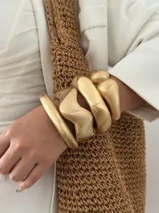 Close-up of minimalist matte gold wavy metal chunky bangles with brushed texture