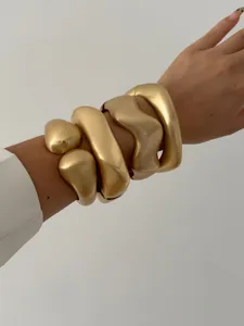 Detailed macro view of stacked matte gold geometric and wavy metal bangles on a wrist