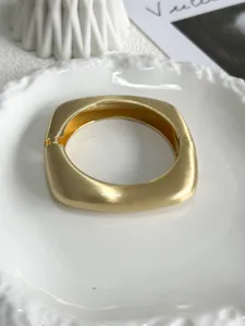 Detailed close-up of a geometric matte gold wavy bangle with brushed metal texture finish