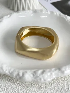 Macro view showing the brushed metal texture of a matte gold geometric wave bangle
