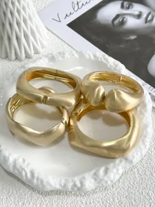 Detailed close-up of matte gold geometric bangles with brushed metal texture details