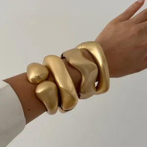Stack of chunky matte gold wave geometric bangles with premium brushed metal finish