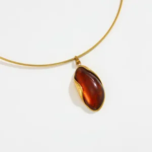 Close-up detail of gold collar necklace featuring irregular amber resin pendant with wavy wrap.