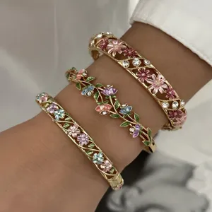 Macro detail view of three gold vintage enamel floral bangles on a female wrist