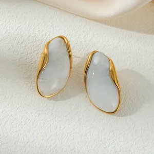 Close-up of irregular wavy gold-plated earrings with white marble effect resin inlay.