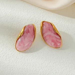 Close-up of pink marbled resin earrings with wavy gold borders on textured surface