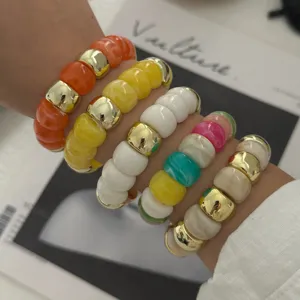 Detailansicht bunter Resin-Perlenarmbänder mit goldenen Trennelementen am Handgelenk.