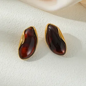 Detailed view of irregular amber earrings with vintage gold wavy edges on textured background.