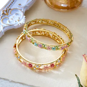 Detailed macro view of hollow gold-tone bangles with colorful enamel flowers and crystals.