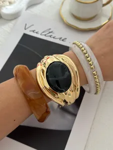 Dettaglio di un bracciale rigido dorato in stile vintage con una grande gemma nera al centro.