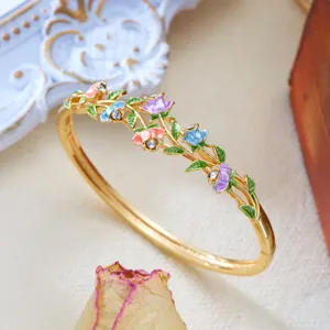 Close-up of a vintage gold bangle featuring colorful enamel flowers and green vines.