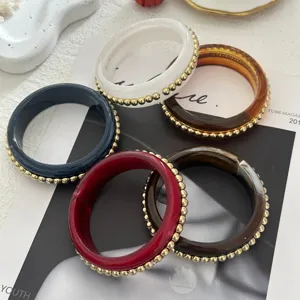 Dettaglio di bracciali vintage in smalto con bordo di perline dorate in cinque colori