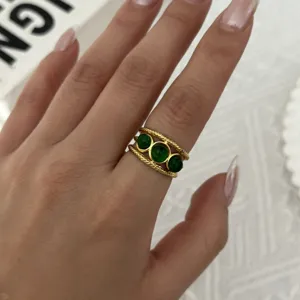 Vista dettagliata di un anello vintage placcato oro con tre pietre verdi smeraldo tonde sulla mano