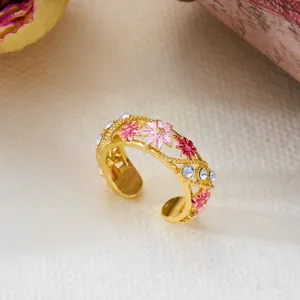 Close-up of a vintage golden open ring featuring pink enamel flowers and sparkling crystals