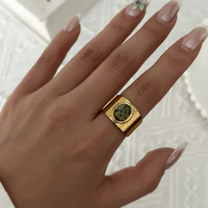Dettaglio di un anello vintage dorato con pietra naturale verde sulla mano di una modella