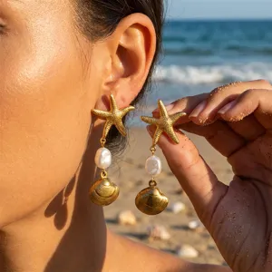 Detailansicht goldener Seestern- und Muschelohrringe mit Perlen am sonnigen Strand