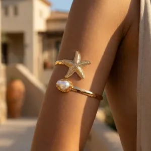 Primo piano del bracciale dorato con stella marina e perla indossato in un resort