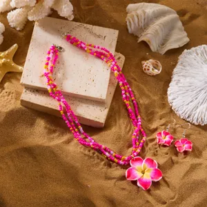 Detailansicht von handgefertigter Frangipani-Halskette und Perlenohrringen auf Sand.