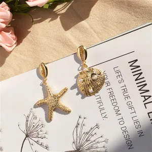 Goldene Seestern- und Muschelohrringe mit Perlen auf minimalistischem Grund.