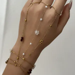Dettaglio di un'elegante catena da mano dorata multistrato con perle e fiori.