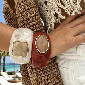 Primo piano di bracciali rigidi in resina stile boho con trama marmorizzata e dettagli dorati.